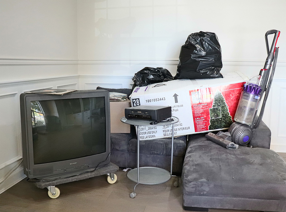 Garage full of junk including furniture and personal items. A red vehicle is also partially seen. 